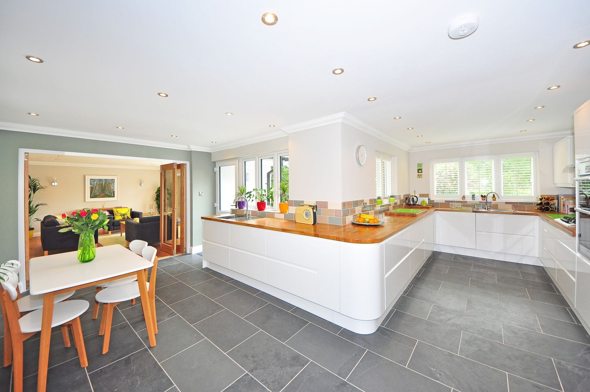 A bright open-plan kitchen with a white gloss run wrapping two walls, a timber breakfast bar and a dining table beyond