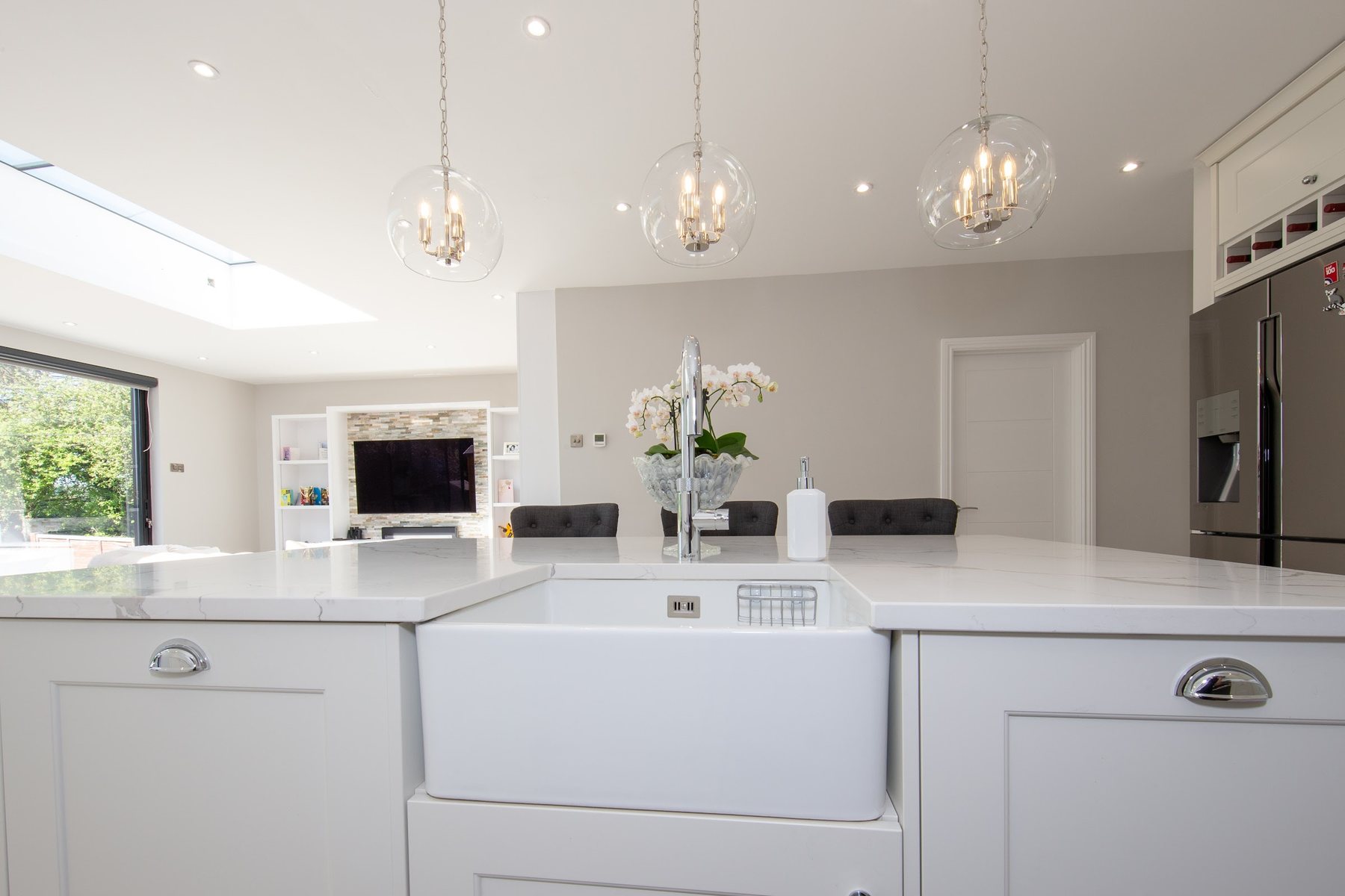 A white shaker island with a butler sink, chrome tap and three glass pendants over a marble-effect worktop
