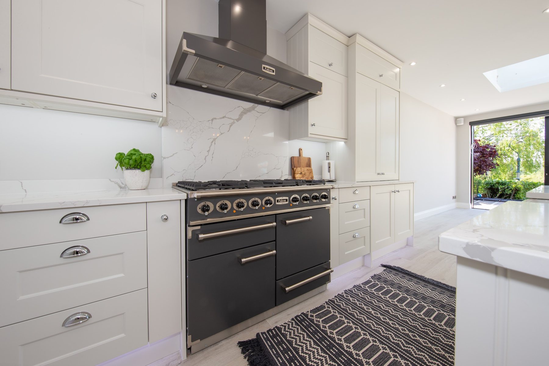 A cream shaker kitchen run with a range cooker, chimney extractor and a marble-effect quartz splashback