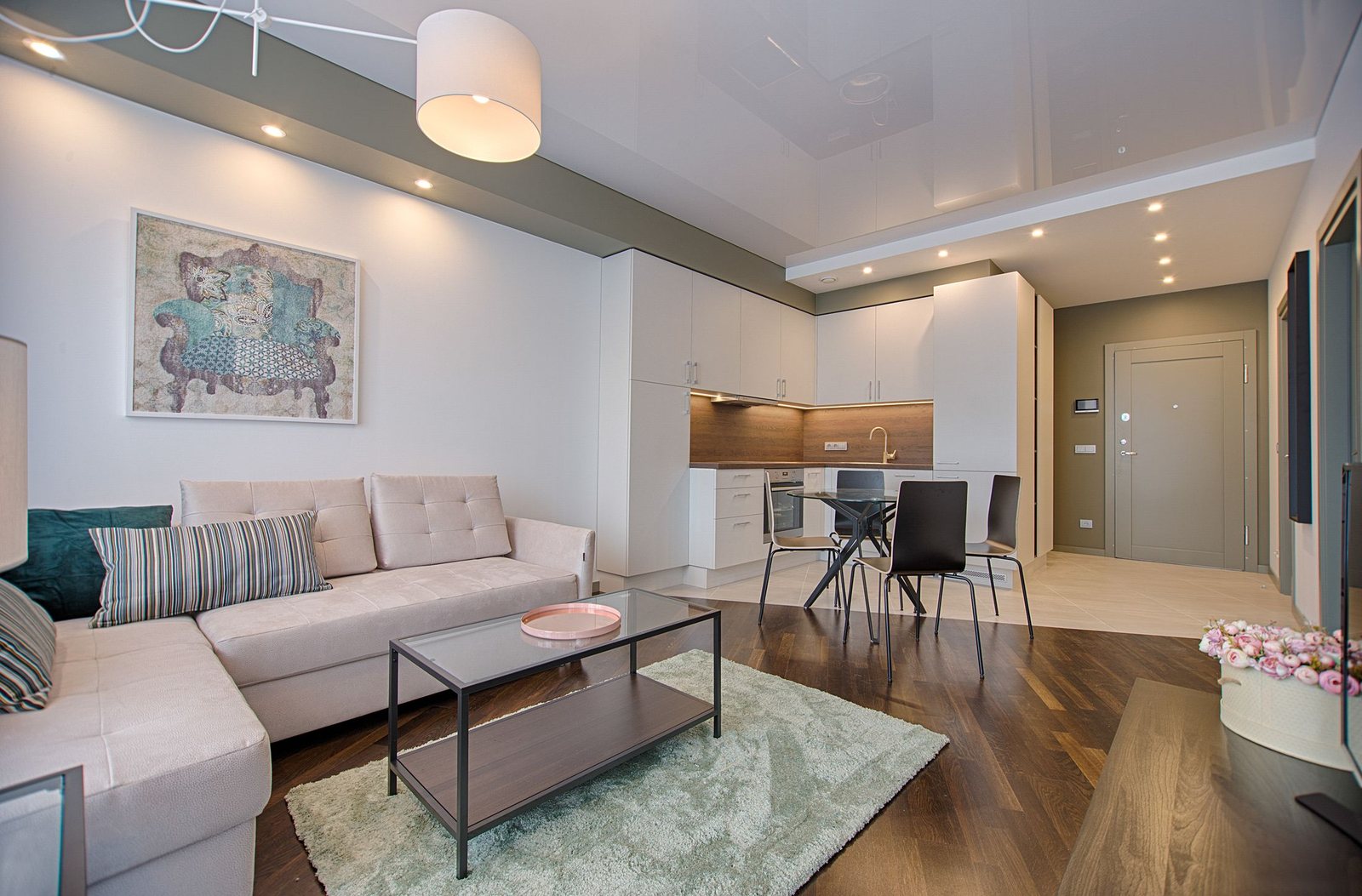 An open-plan living room and kitchen with a dining table under a pendant and a long pale sofa
